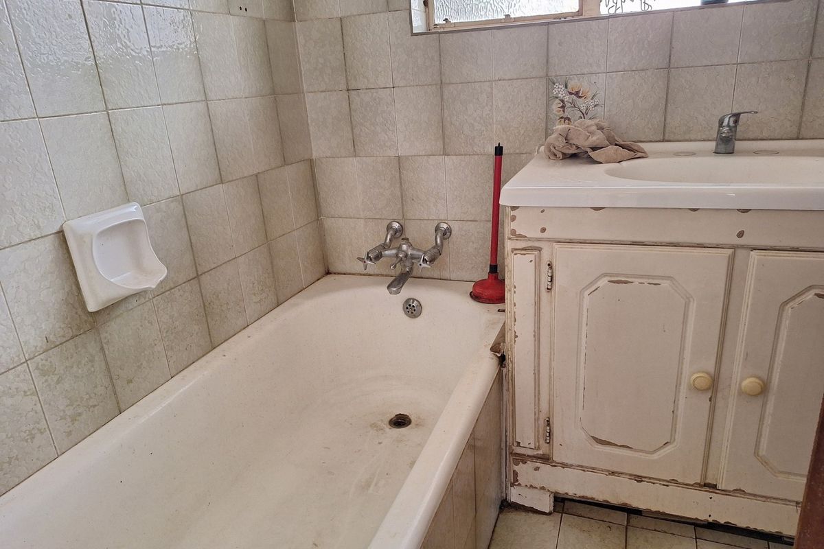 A dated bathroom featuring a standard bathtub, basin, and vanity cabinet with visible wear on the cabinetry and wall tiles.