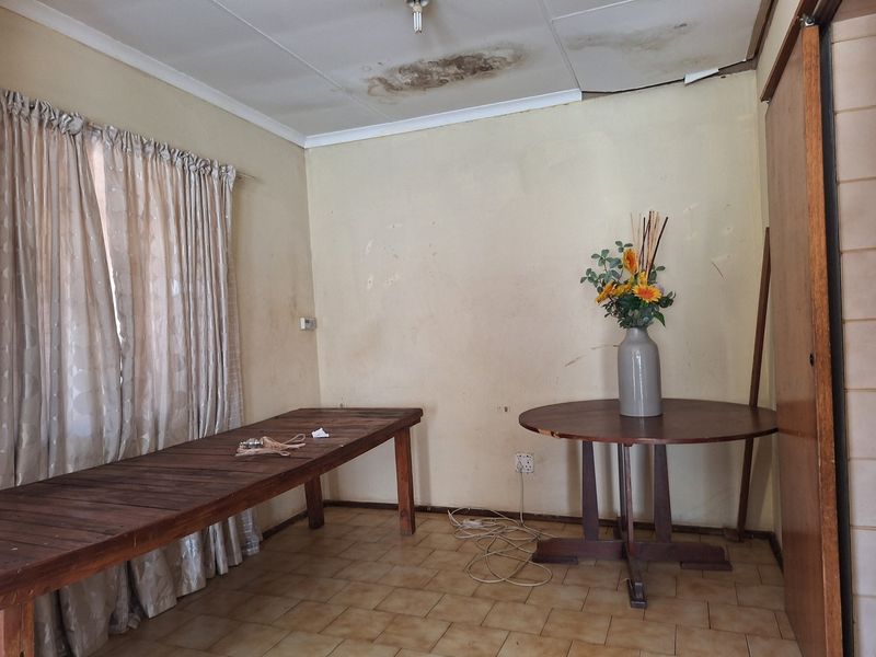 A bedroom featuring tiled flooring and a built-in cupboard, currently showing significant signs of ceiling water damage and general wear requiring renovation.