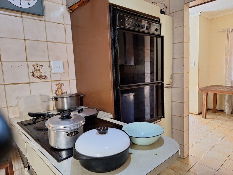 A dated kitchen featuring a built-in oven, electric hob, and tiled backsplash, offering potential for a modern renovation.