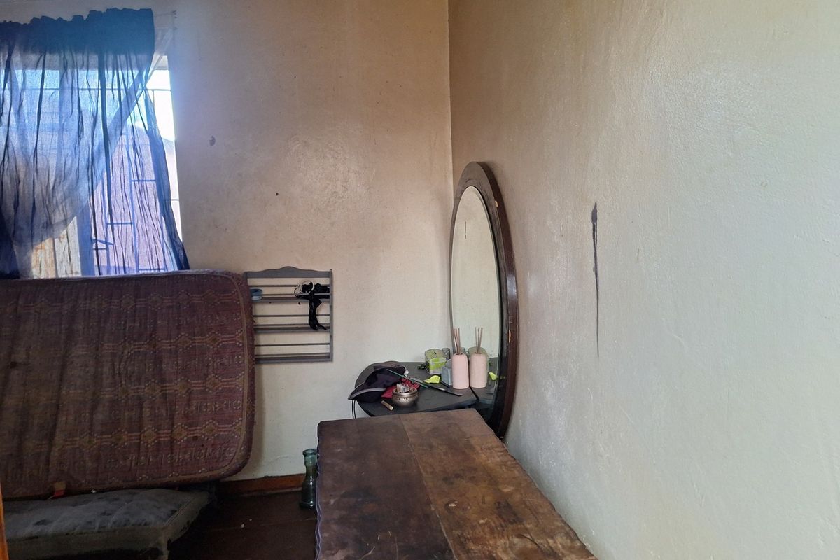 A bedroom interior featuring a window with security bars and walls showing signs of wear and staining, requiring cosmetic updates.