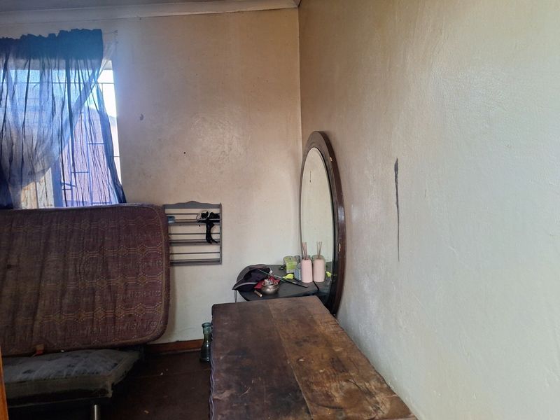 A bedroom interior featuring a window with security bars and walls showing signs of wear and staining, requiring cosmetic updates.