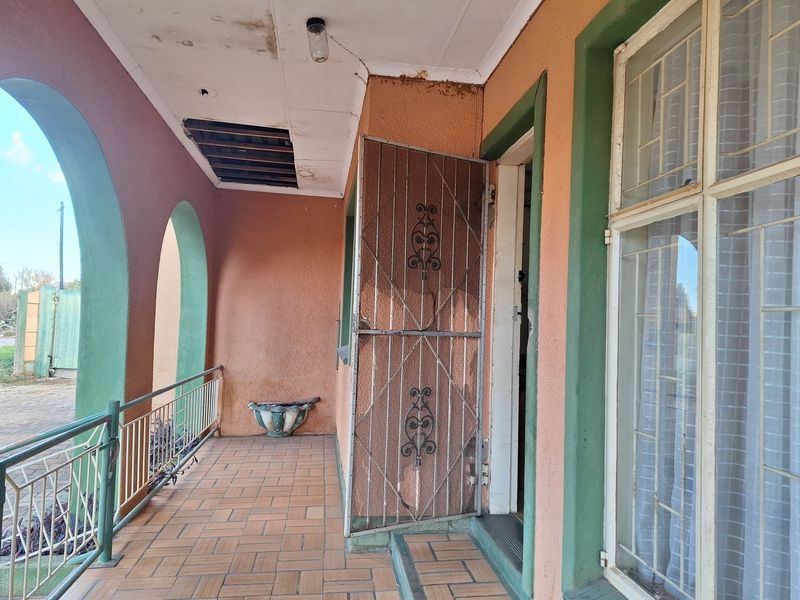 A covered patio area featuring arched pillars, tiled flooring, and a metal security gate, requiring some maintenance to the ceiling and plasterwork.