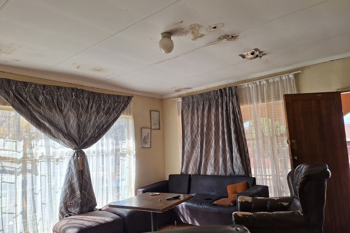 Living room area featuring large windows with curtain rails and visible water damage on the ceiling panels requiring repair.