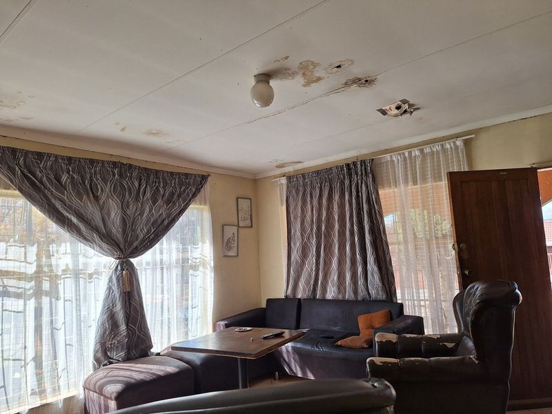 Living room area featuring large windows with curtain rails and visible water damage on the ceiling panels requiring repair.