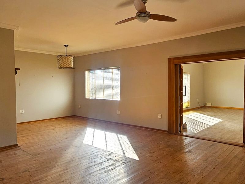 Spacious, empty living area featuring original wooden flooring, a ceiling fan, and a large wooden doorway leading to an adjacent room.