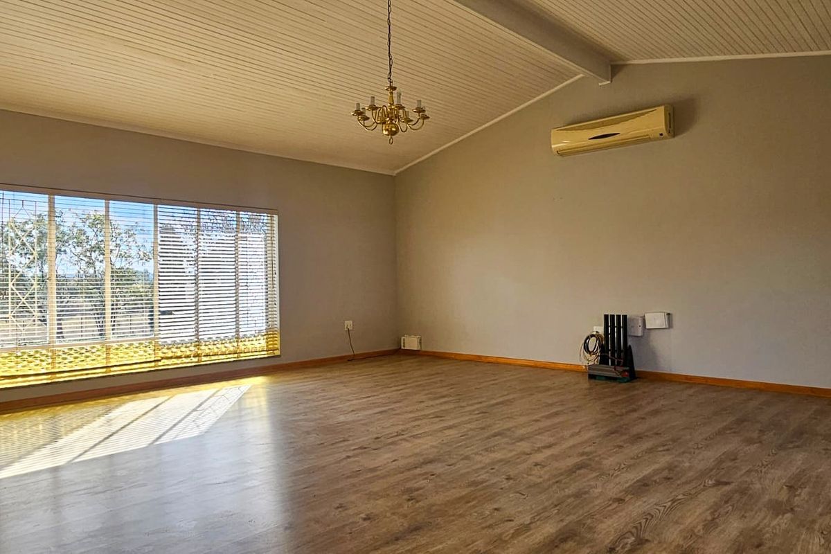 Spacious living area featuring vaulted timber ceilings, laminate flooring, and a wall-mounted air conditioning unit, offering a bright and open atmosphere.