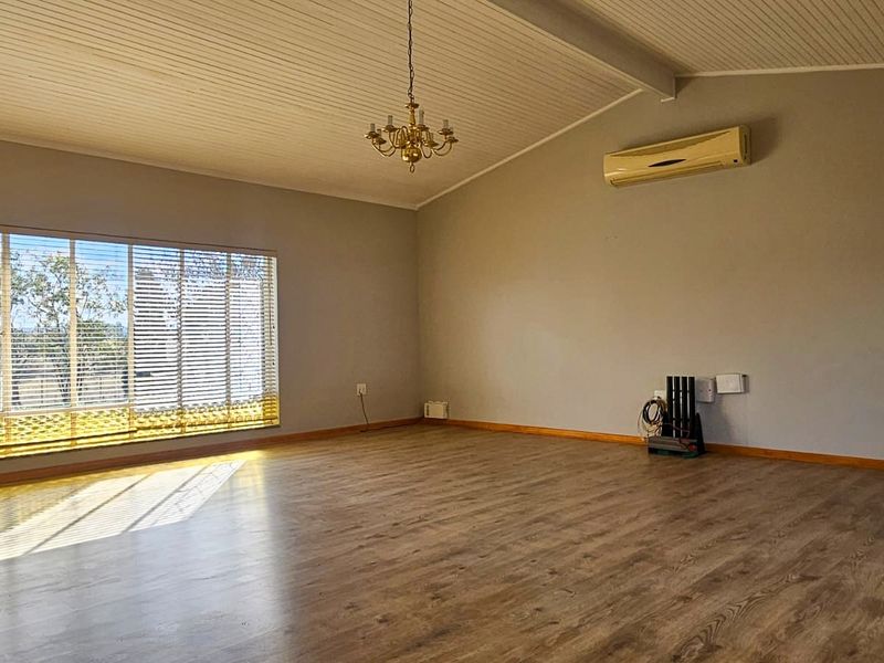 Spacious living area featuring vaulted timber ceilings, laminate flooring, and a wall-mounted air conditioning unit, offering a bright and open atmosphere.