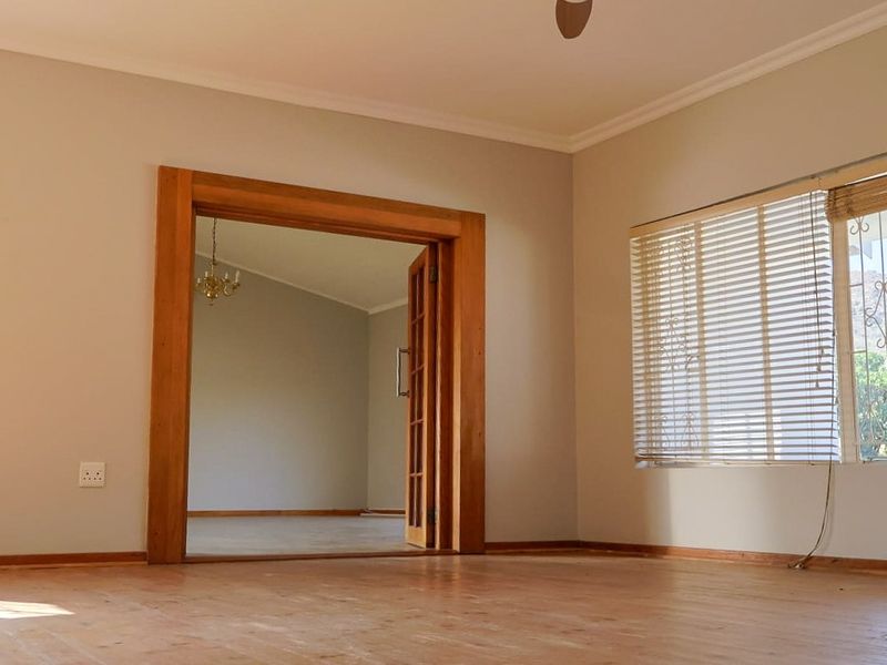 Spacious living area featuring warm wooden flooring, a ceiling fan, and classic wooden door frames leading to an adjacent room.