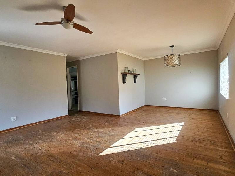 Spacious living area featuring original hardwood flooring, ceiling fan, and neutral wall tones, offering a blank canvas for interior design.