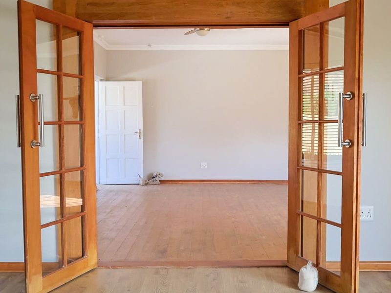 An empty living room featuring wooden flooring and classic wooden french doors, providing a bright and open space ready for personalization.