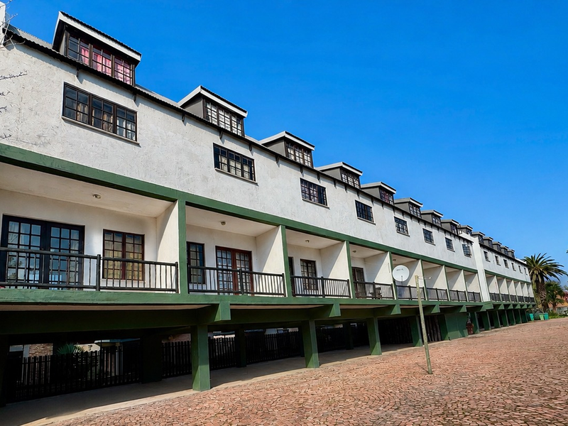 Exterior view of a multi-story apartment complex featuring a row of balconies with metal railings and dormer windows along the roofline.