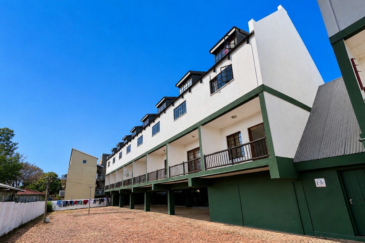 Exterior view of an apartment complex featuring a paved courtyard, multiple balconies with metal railings, and a multi-level facade.