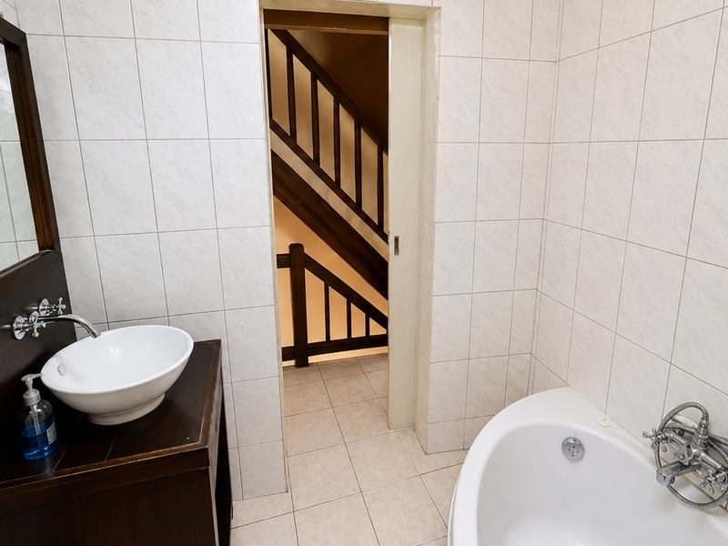 A functional bathroom featuring a vessel sink, vanity, and bathtub with tiled finishes, providing access to an adjacent staircase area.