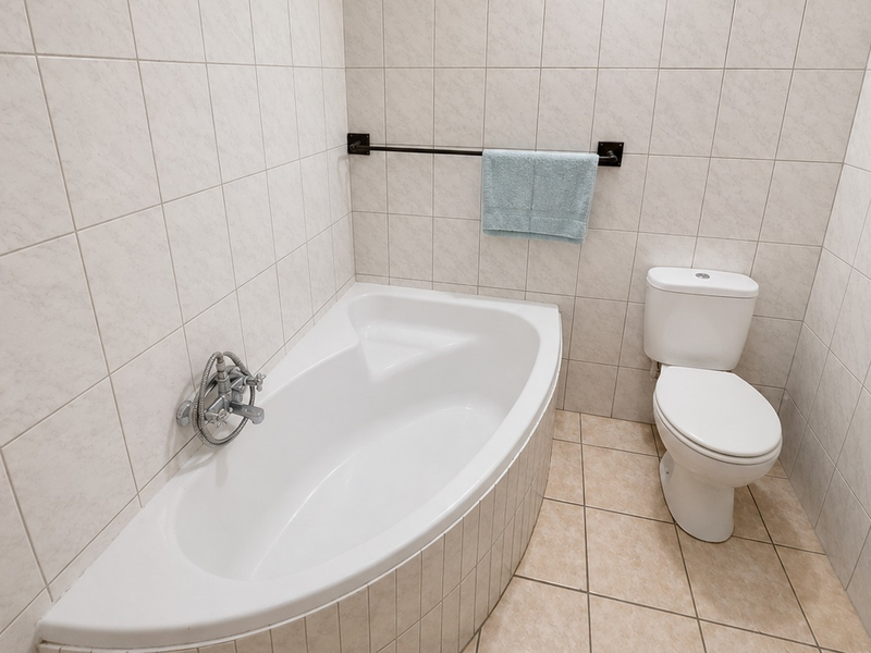 A functional bathroom featuring a corner bathtub, a standard toilet, and neutral wall and floor tiling.