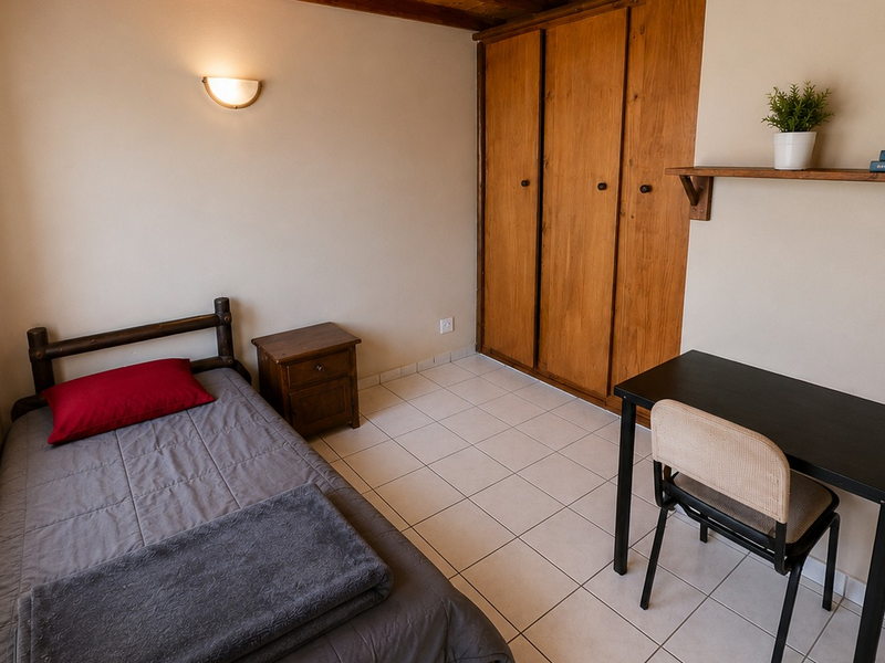 A functional bedroom featuring tiled flooring, a built-in wooden wardrobe, and a wall-mounted light fixture, offering a practical and well-maintained living space.