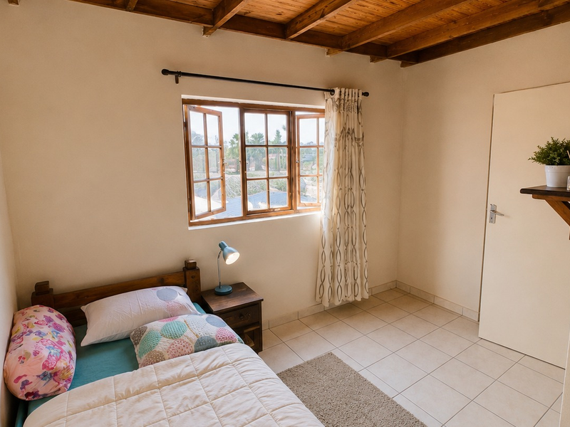 A cozy bedroom featuring exposed timber ceiling beams, tiled flooring, and a timber-framed casement window providing natural light.