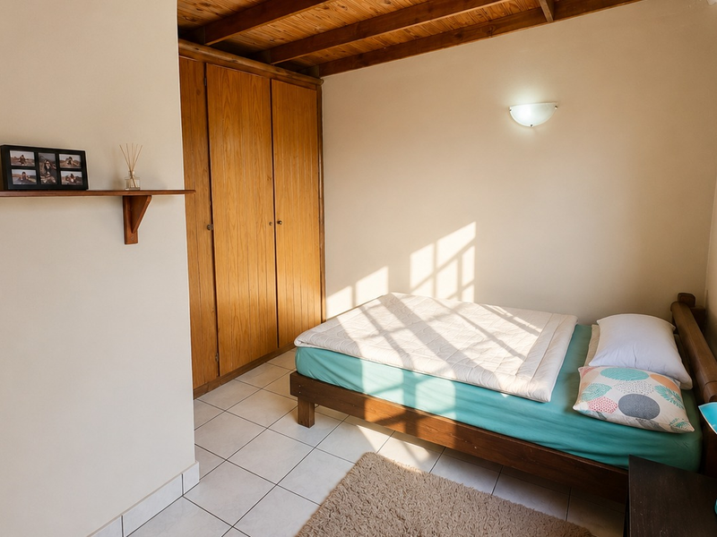 A bedroom featuring tiled flooring, exposed timber ceiling beams, and a built-in wooden wardrobe, offering a warm and functional living space.