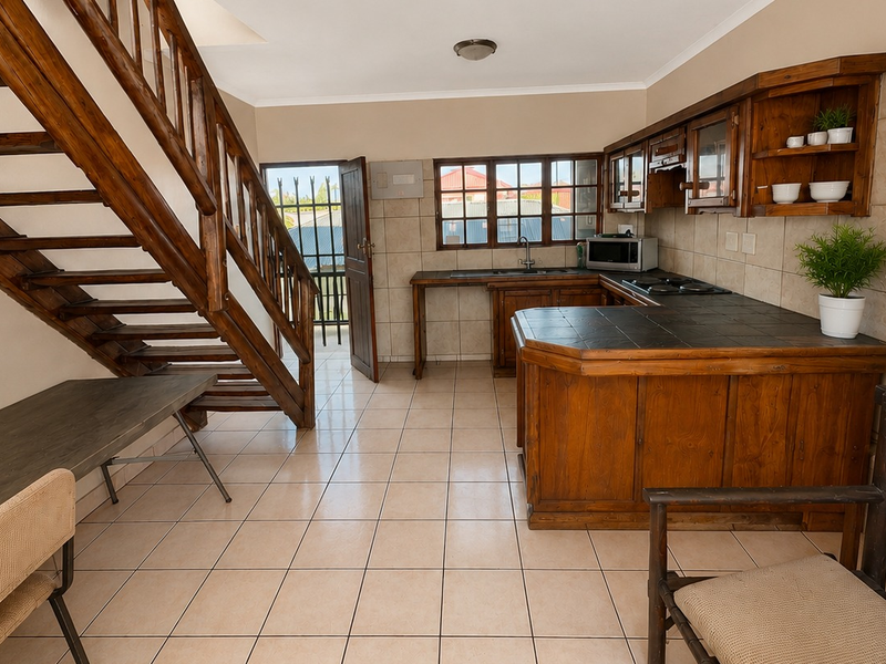 Open-plan kitchen area featuring wooden cabinetry, tiled countertops, and a prominent wooden staircase leading to the upper level.
