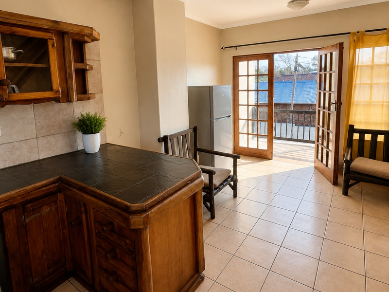 Open-plan kitchen and living area featuring rustic wooden cabinetry, tiled countertops, and direct access to a private balcony through double doors.
