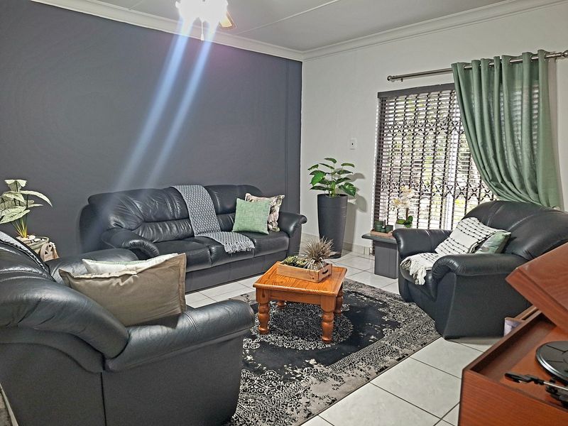 A comfortable living room featuring tiled flooring, a ceiling fan, and a security gate over the window, providing a functional and well-maintained space.