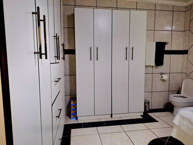 A functional bathroom featuring extensive built-in white cabinetry for storage, tiled walls and flooring, and standard sanitary fixtures.