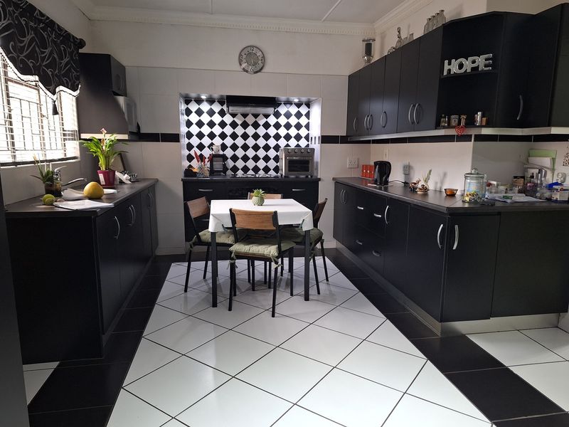 A well-maintained kitchen featuring black cabinetry, a contrasting checkered backsplash, built-in cooking appliances, and tiled flooring throughout.