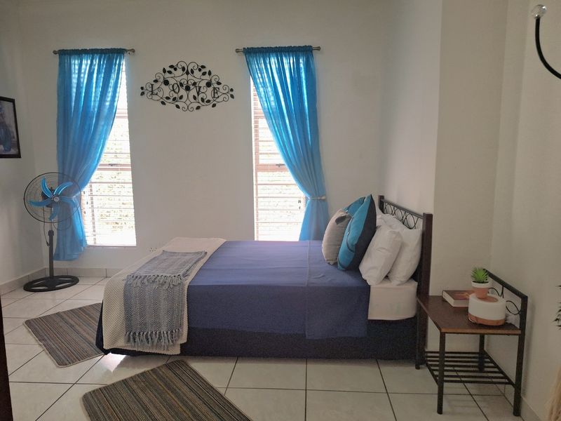A functional bedroom featuring tiled flooring and dual windows fitted with venetian blinds, providing natural light to the space.