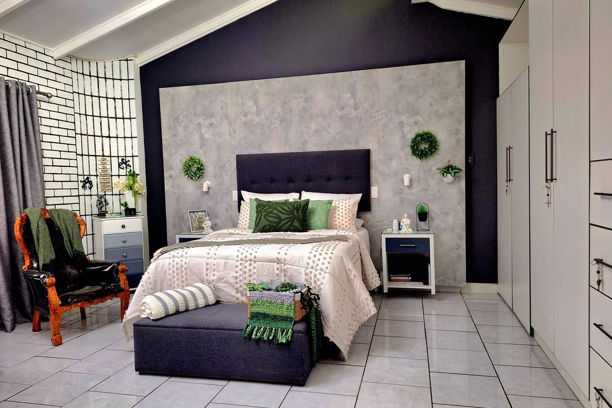 Spacious bedroom featuring a vaulted ceiling, modern tiled flooring, a decorative feature wall, and ample built-in cupboard storage.