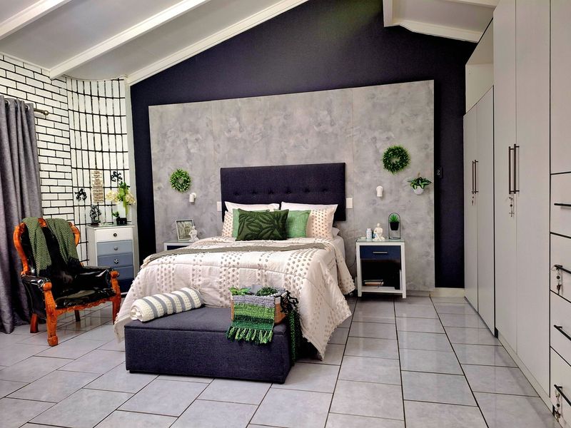 Spacious bedroom featuring a vaulted ceiling, modern tiled flooring, a decorative feature wall, and ample built-in cupboard storage.