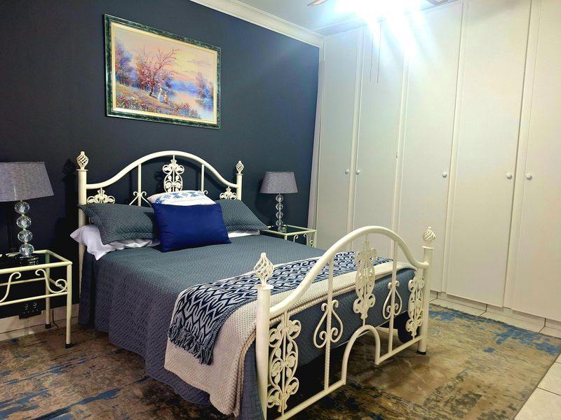 A well-maintained bedroom featuring dark accent walls, built-in floor-to-ceiling cupboards, and a ceiling fan.