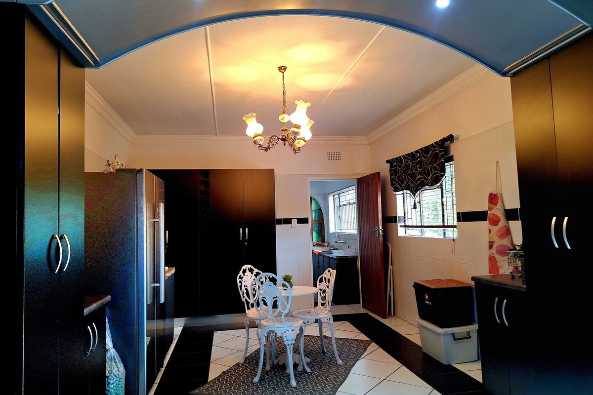 A spacious kitchen featuring dark built-in cabinetry, contrasting black and white tiled flooring, and an arched entryway leading to a secondary prep area.