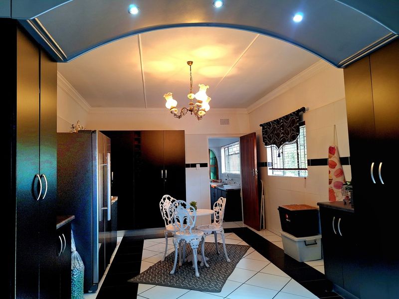 A spacious kitchen featuring dark built-in cabinetry, contrasting black and white tiled flooring, and an arched entryway leading to a secondary prep area.