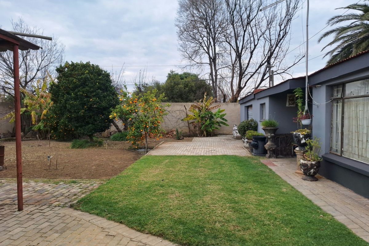A rear garden area featuring a paved patio, a well-maintained lawn, and a perimeter boundary wall.