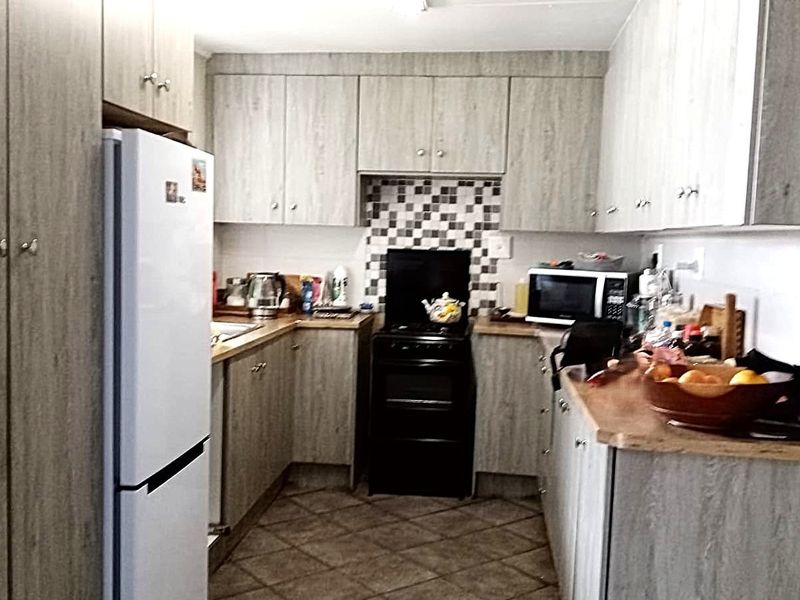 A functional kitchen featuring wood-look laminate cabinetry, tiled backsplash, and durable tiled flooring, providing a practical workspace with ample storage.