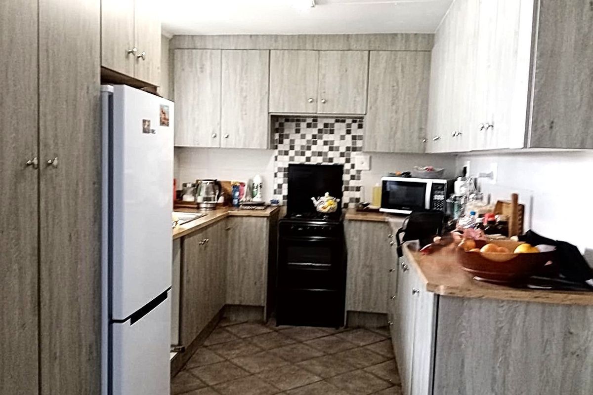 A functional kitchen featuring wood-look laminate cabinetry, tiled backsplash, and durable tiled flooring, providing a practical workspace with ample storage.