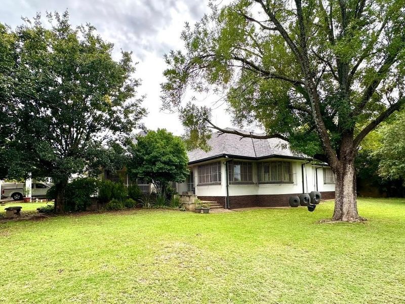 A view of the rear elevation of the house featuring a large garden, mature trees, and security bars on the windows.