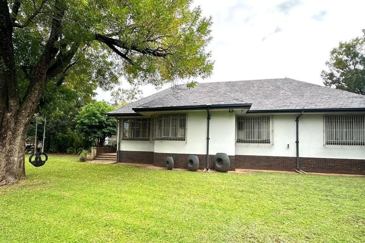 Rear view of the house featuring a tiled roof, brick base, and security bars on the windows, set against a spacious lawn.