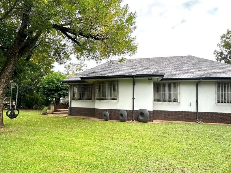 Rear view of the house featuring a tiled roof, brick base, and security bars on the windows, set against a spacious lawn.