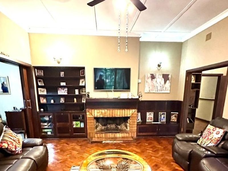 A living room featuring a brick fireplace, built-in wooden shelving, and classic parquet flooring, offering a traditional and cozy atmosphere.