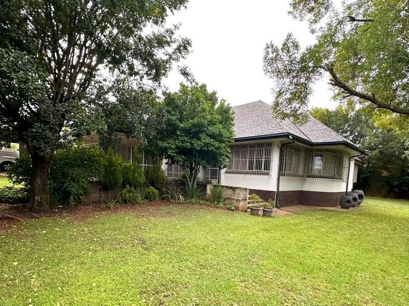 Rear view of the house featuring a large garden, mature trees, and security bars on the windows.