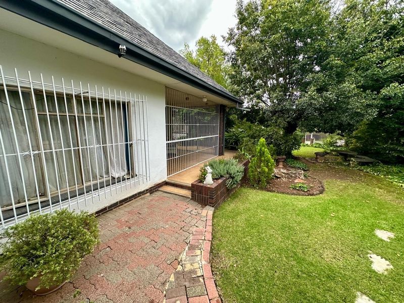 Rear exterior view featuring a paved patio area, brick planter, and security bars on the windows, overlooking a landscaped garden.