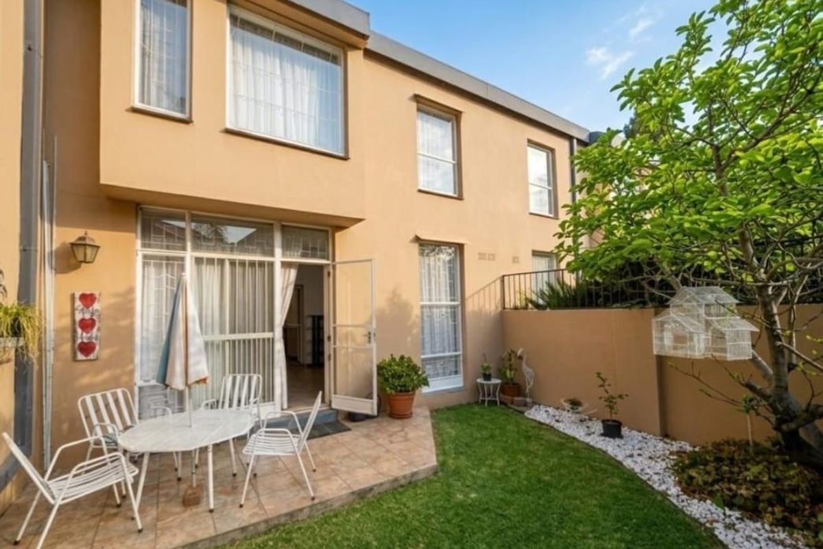 Rear view of the townhouse featuring a paved patio area, small private garden, and direct access to the interior through sliding glass doors.