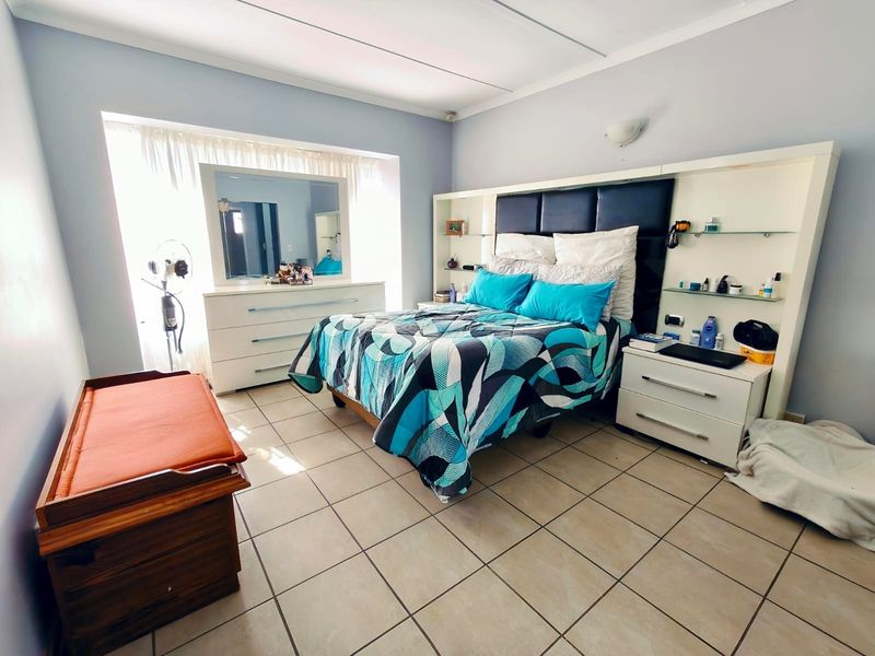 A bedroom featuring tiled flooring, a built-in headboard unit with integrated shelving, and a large window allowing natural light.