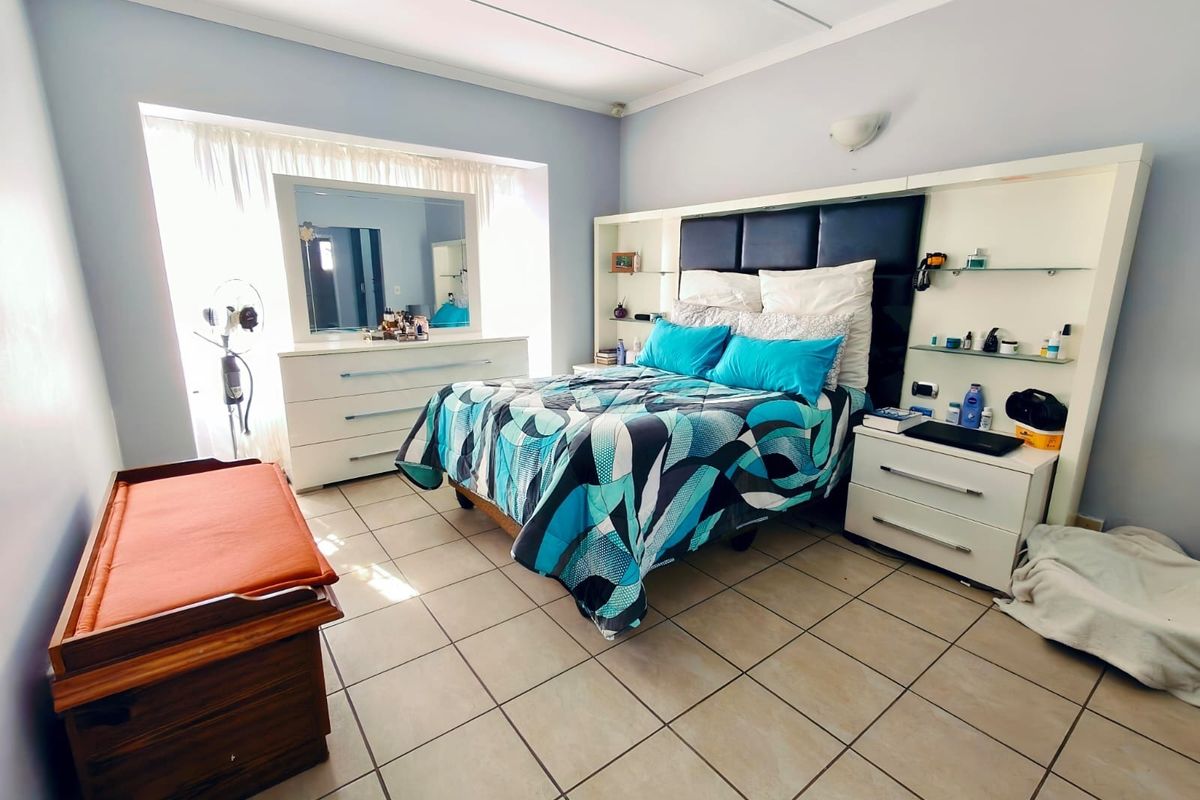 A bedroom featuring tiled flooring, a built-in headboard unit with integrated shelving, and a large window allowing natural light.