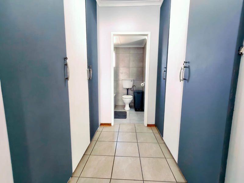 A clean hallway featuring built-in cupboards with modern two-tone doors, leading directly into a tiled bathroom space.