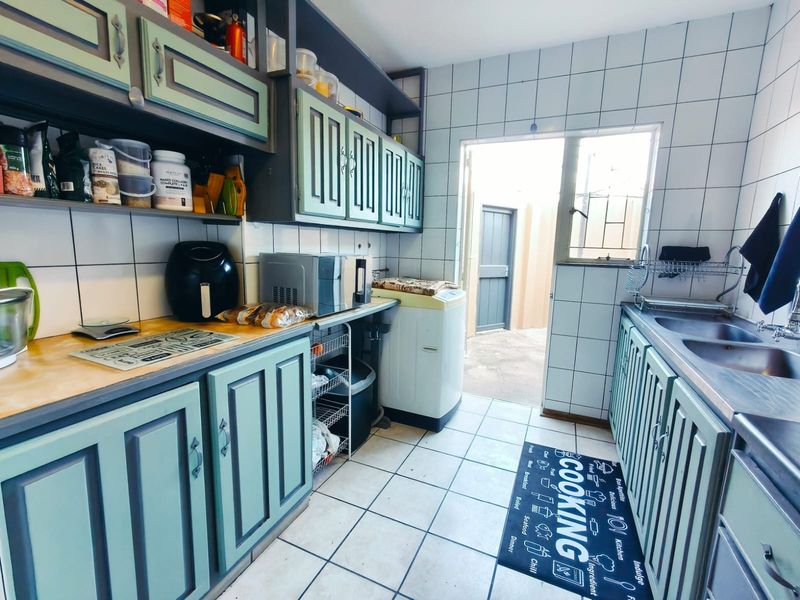 Functional kitchen featuring built-in cabinetry, double basin sink, and tiled finishes with direct access to an exterior courtyard area.