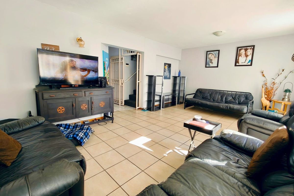 Spacious living room featuring neutral ceramic tile flooring and direct access to an internal staircase with a security gate.