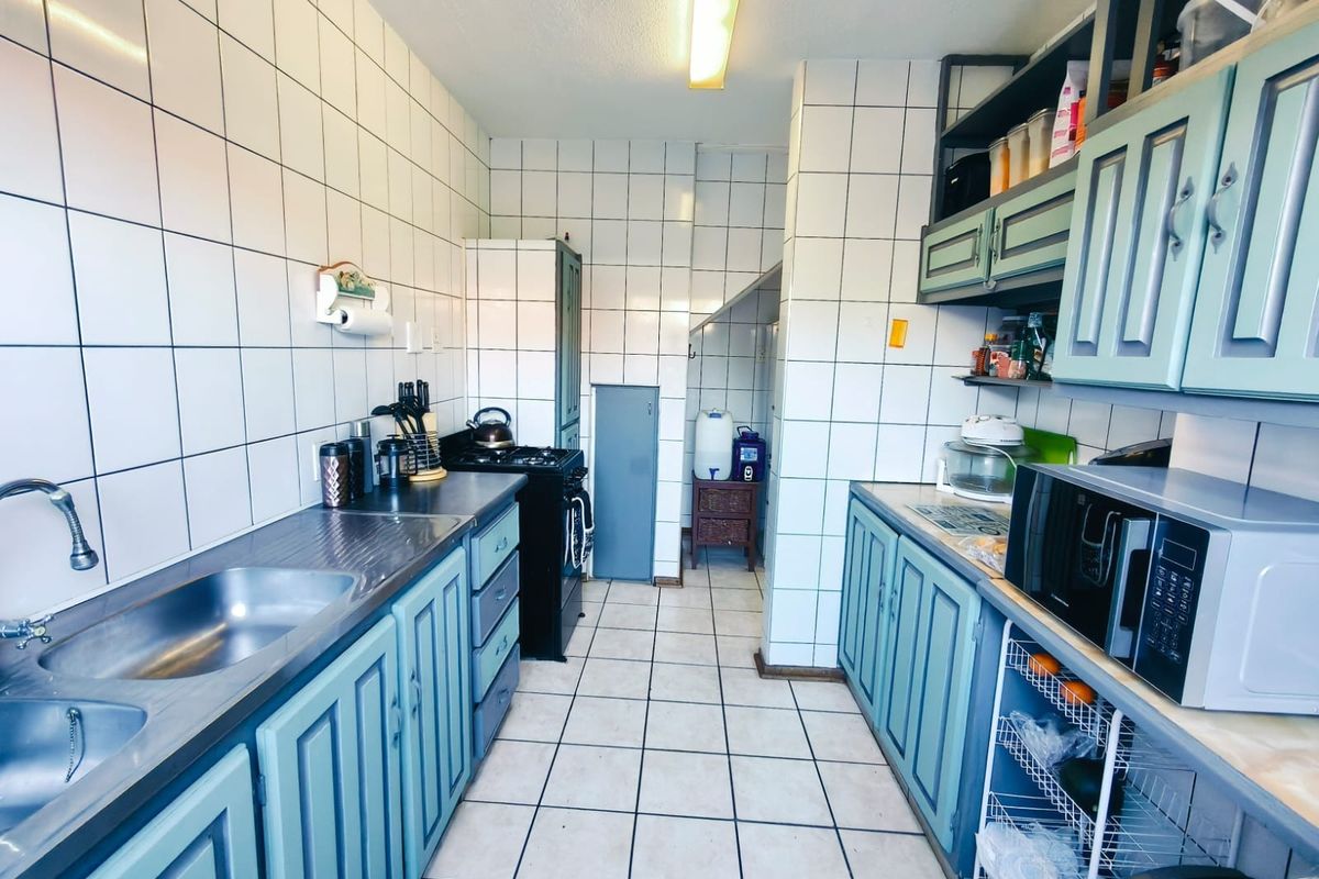 A functional galley-style kitchen featuring tiled walls, built-in cabinetry, a double stainless steel sink, and a gas stove.
