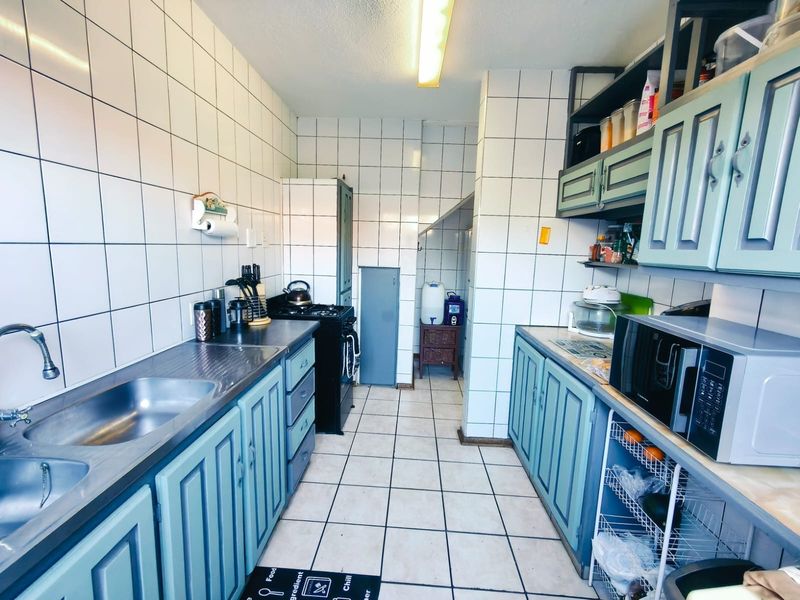 A functional galley-style kitchen featuring tiled walls, built-in cabinetry, a double stainless steel sink, and a gas stove.