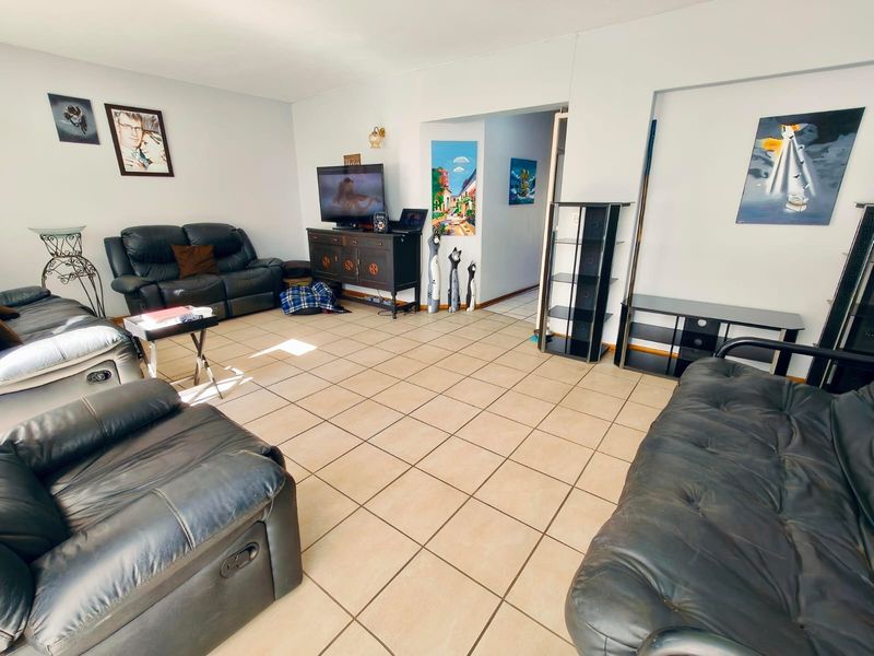 A spacious living room featuring neutral ceramic tile flooring and access to an adjoining hallway.